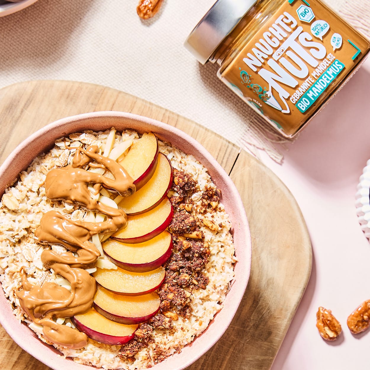 Bio Mandelmus Gebrannte Mandel in einem Glas neben einer Schüssel Haferflocken mit Obst