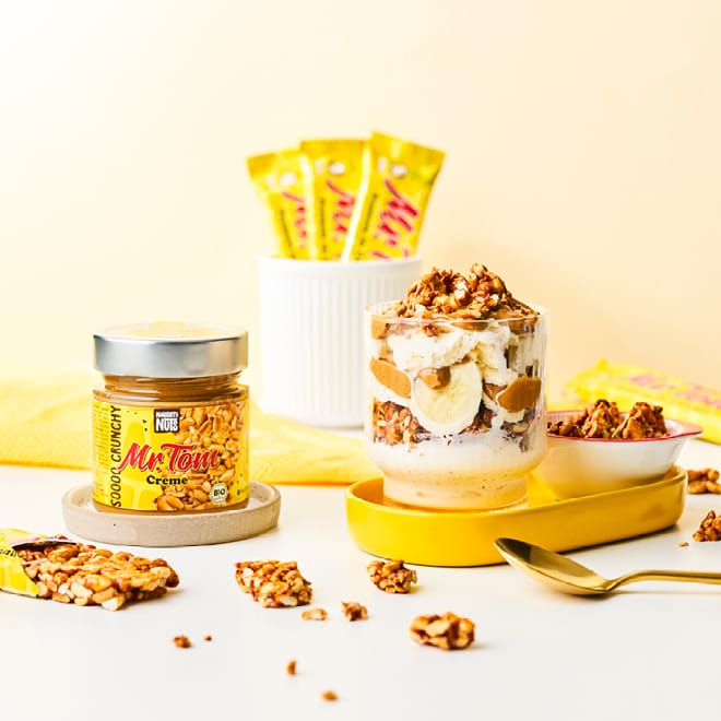 Mr Tom Creme Glas mit Banane und Müsli, daneben Erdnussriegel und Mr Tom Creme Glas